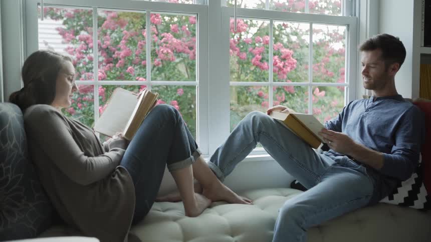 Man and woman sit on a sofa each reading a book