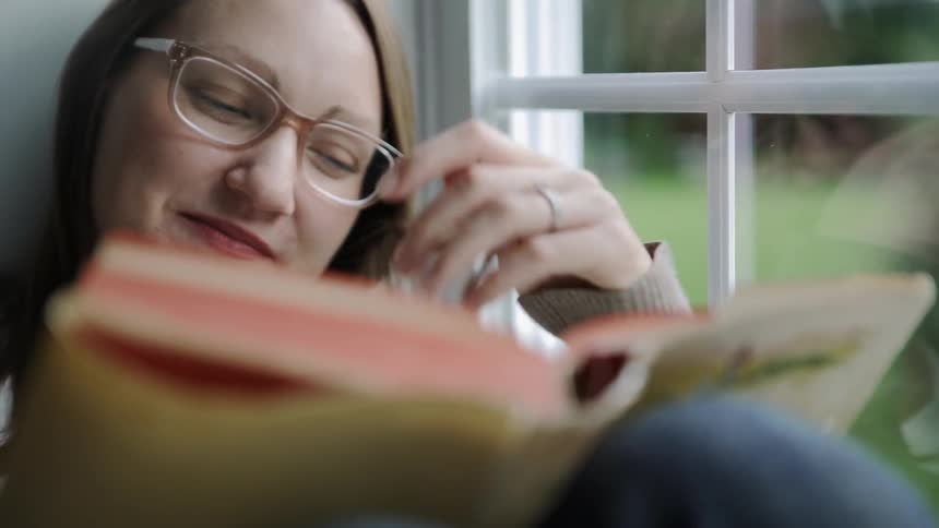 Woman smiles as she twirls her hair and reads a book