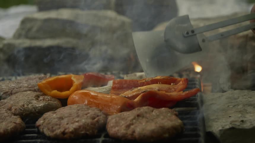 The man flips some peppers on the smokey grill