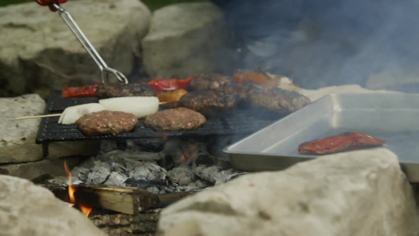 A man moves peppers off a grill and onto a sheet pan outside