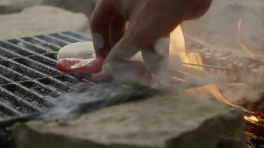 Man sets a red pepper on a hot grill