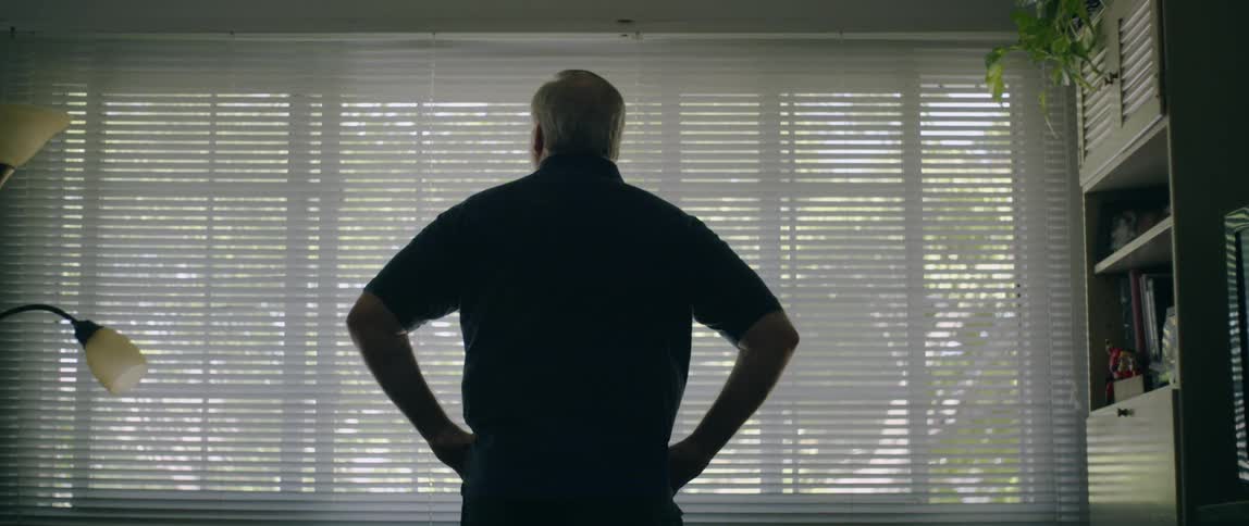 A man stands in front of a large window at day time with his hands on his hips