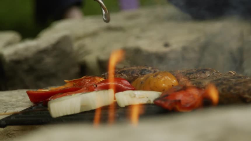 A man moves a burger on a grill using tongs