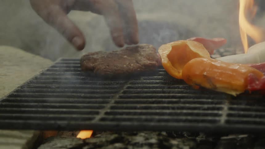 Man places a burger on the hot grill with his bare hands