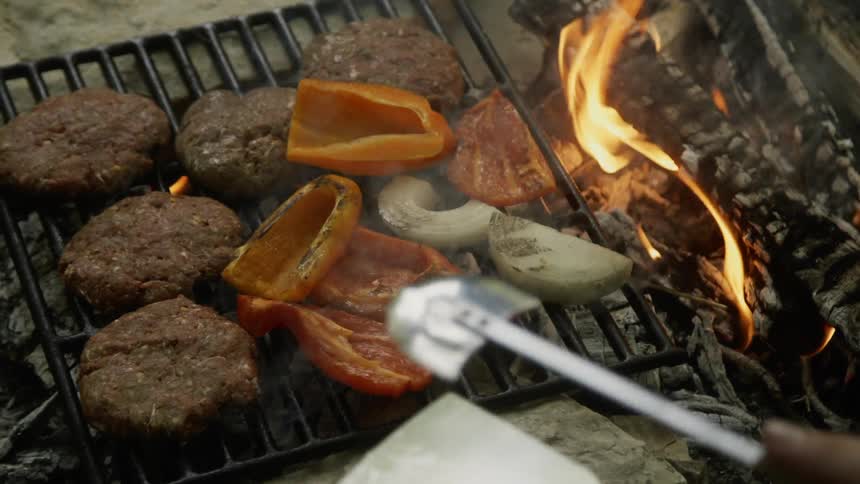 Peppers, burgers and onions cooking on a flaming grill