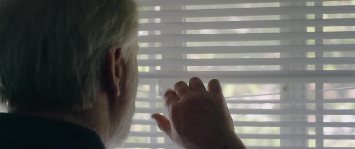 Elderly man moves window blinds to look out the window