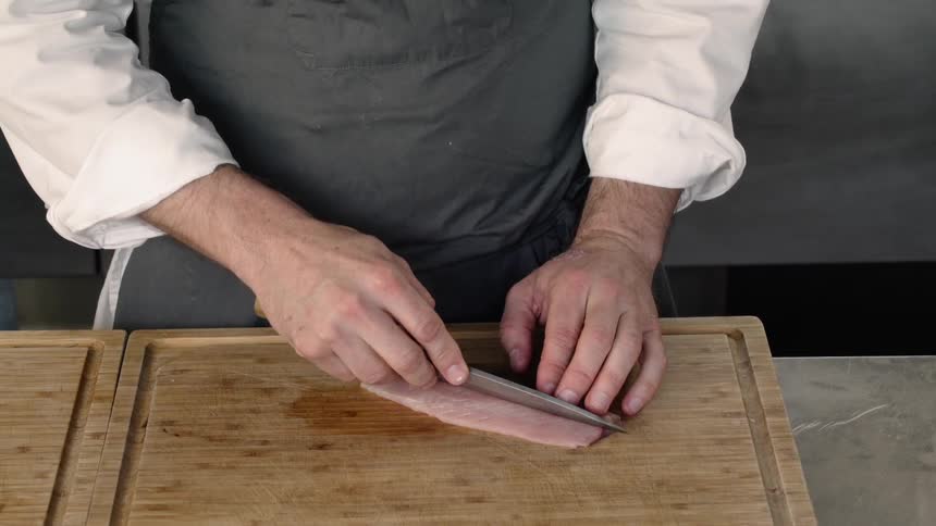 Person cuts a piece of fish on a wooden cutting board