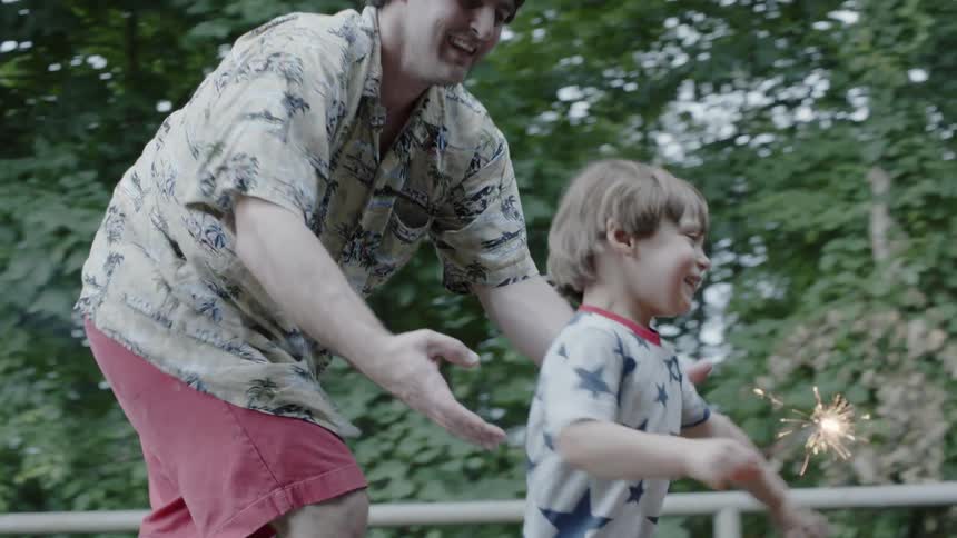 A dad chases his son who is running with a sparkler