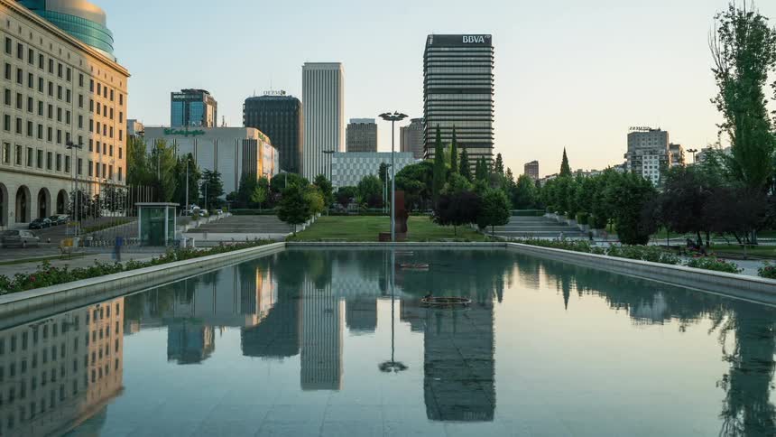 Many people walk past a large pool of water in the city