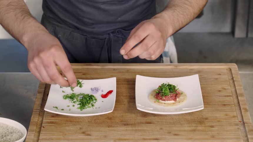 A chef adds garnish to an appetizer on a plate