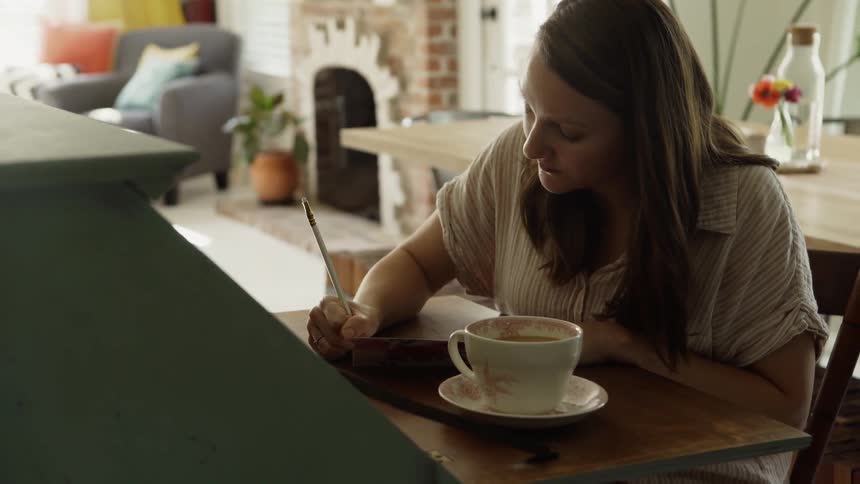A woman writes with a drink at her desk