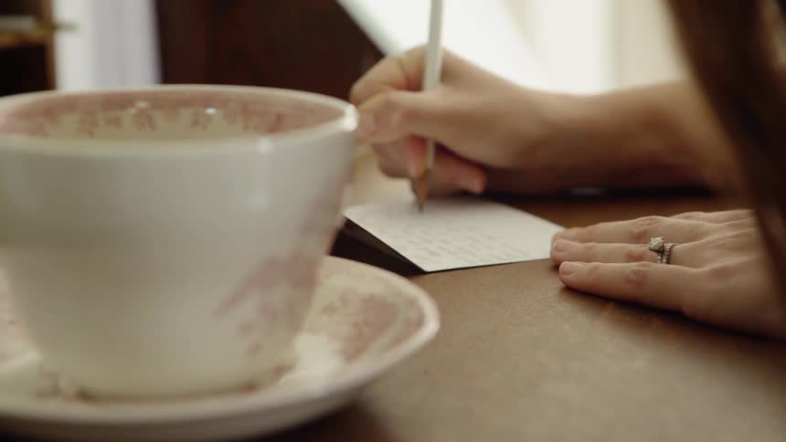 A woman writes a note at a desk with a tea cup next to her