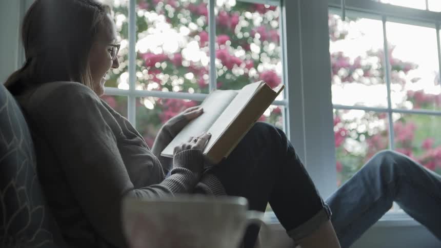 Steam Rises From Hot Drink While Woman Reads in Window