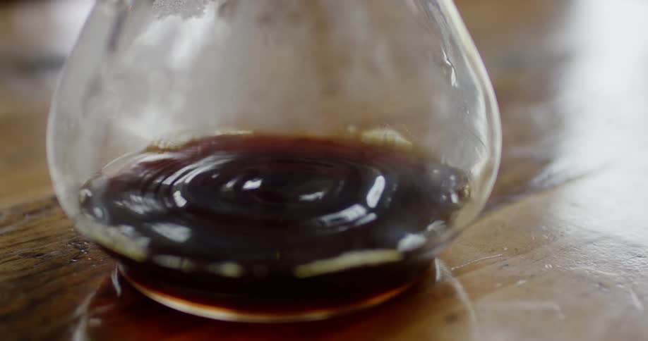 A brown liquid is dripping into a large glass container