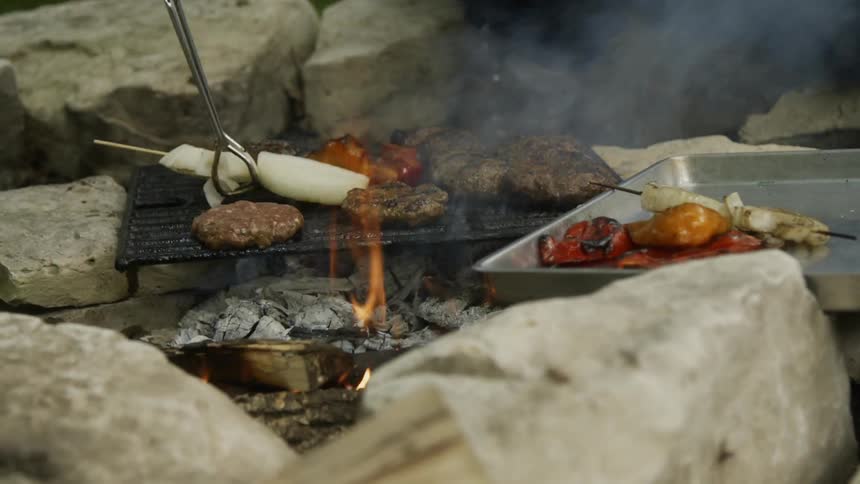 Person uses tongs to flip burgers over on a grill