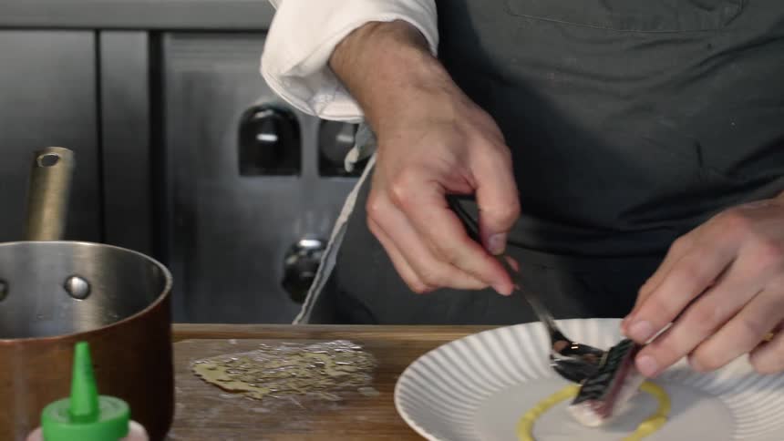 Chef spoons a small portion of fish onto a plate
