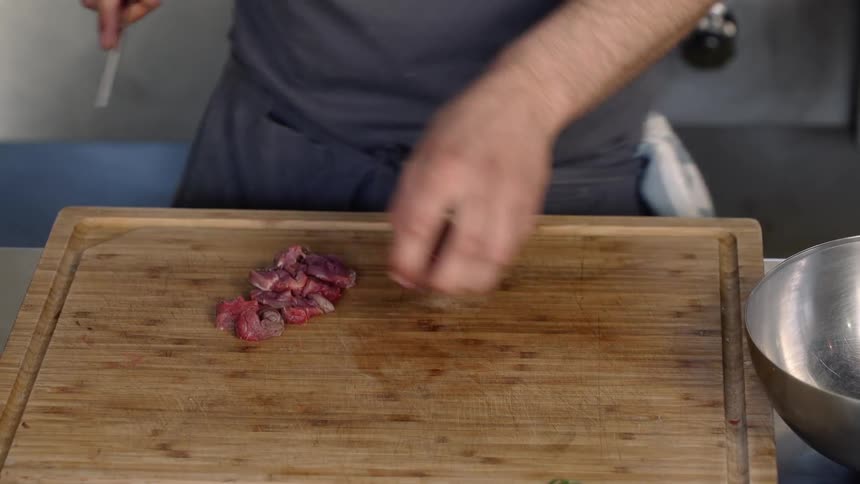 A chef cutting a piece of meat to fine pieces