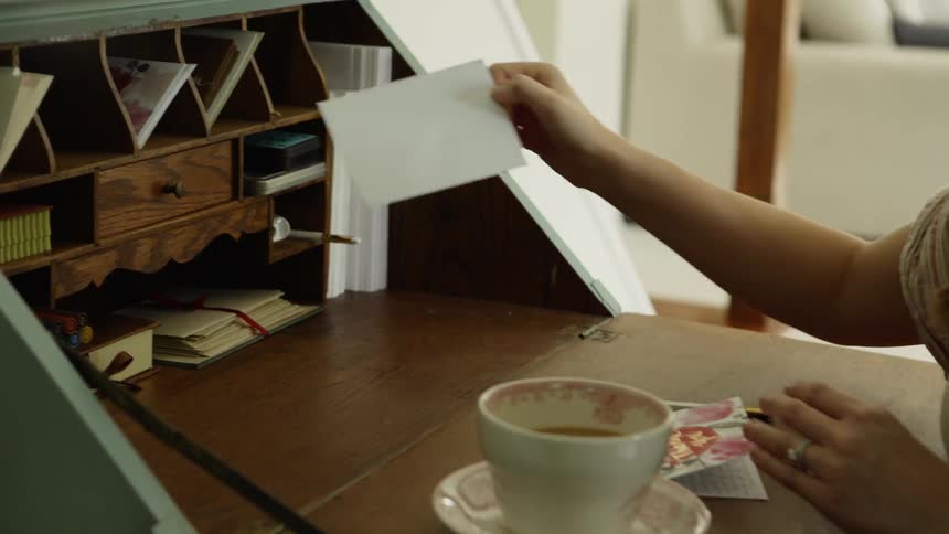 A woman sits at a secretary desk and takes out an envelope to put a card in