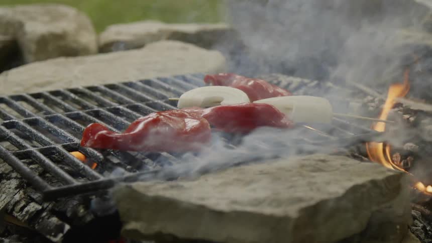 Person puts a pepper on a smoking grill