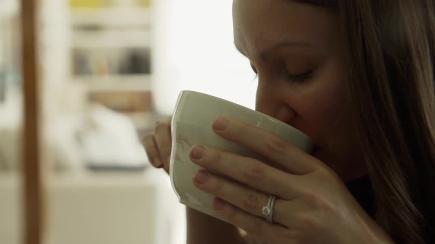 The woman is smiling as she drinks from the mug