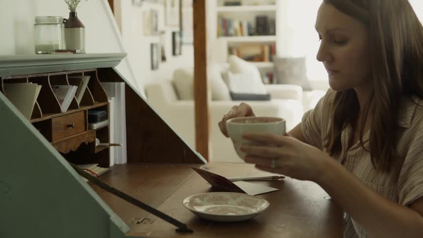 A woman takes a sip from her cup while sitting at a desk