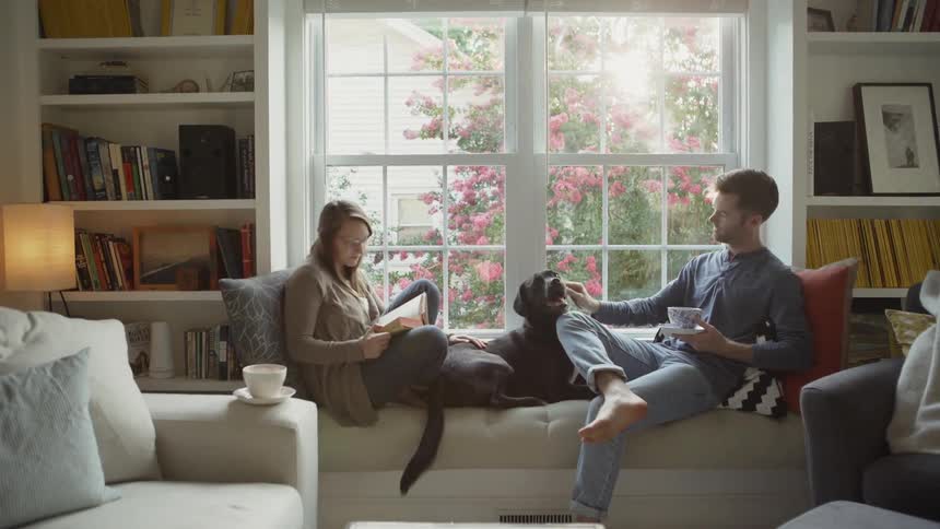 The dog sits between the two people sitting on the windowsill