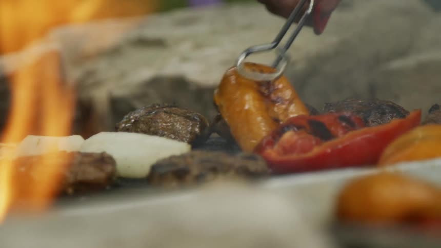 A person holding tongs flips peppers on a grill