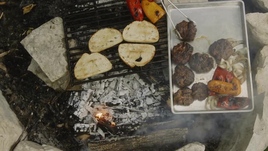 Man uses tongs to move the burgers in the pan sitting on a hot grill
