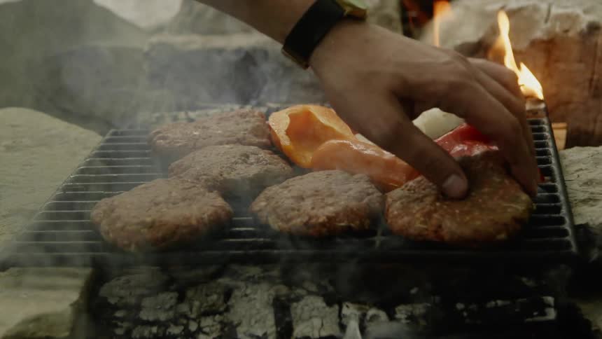 The person places some burgers on the grill