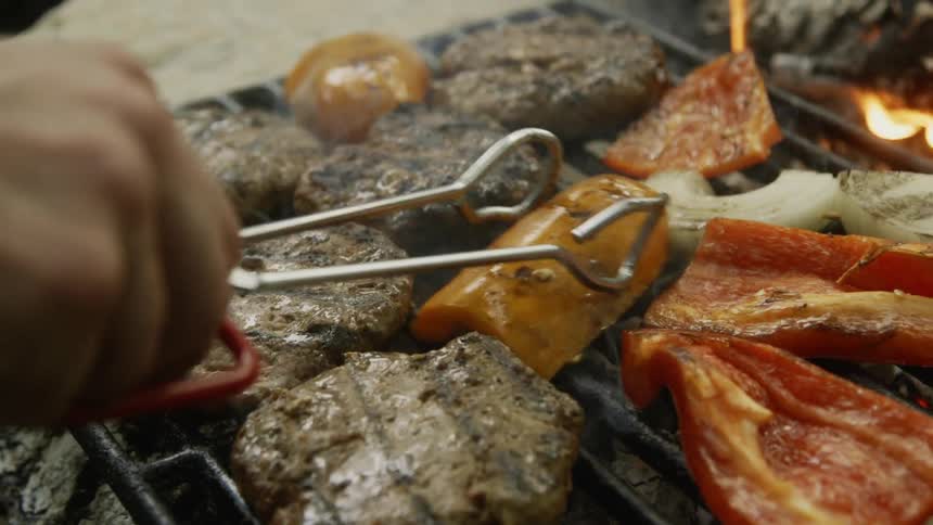 Man uses tongs to flip over the food on the grill