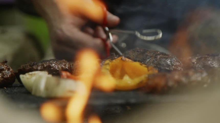 Person uses tongs to flip food over on a smoking grill