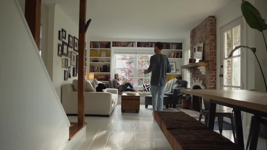 Man carries a mug into the living room and give it to a woman