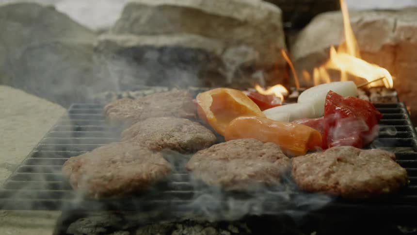 Food sizzles on a grill rack above a smoking fire