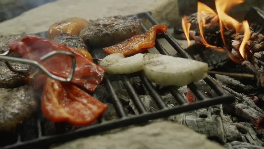 Tongs flip a red pepper over on a smoking grill
