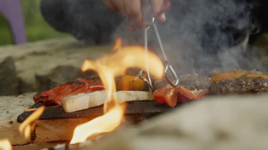 Person moves food around on a grill with tongs