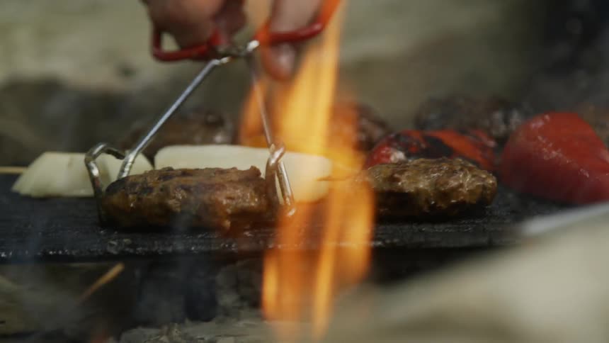 Man uses tongs to flip the food on the hot grill