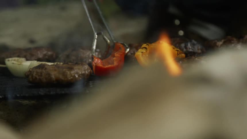 Tongs are used to flip peppers on a flaming grill