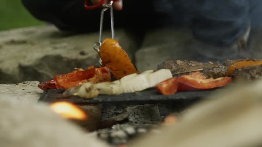 A person is flipping meat and veggies on the grill
