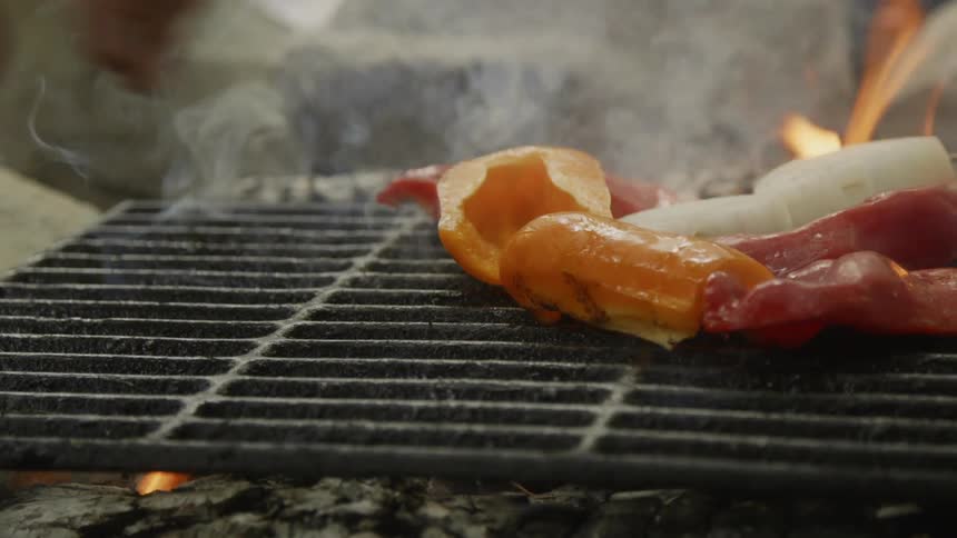 A man arranges peppers on an outdoor grill with flames