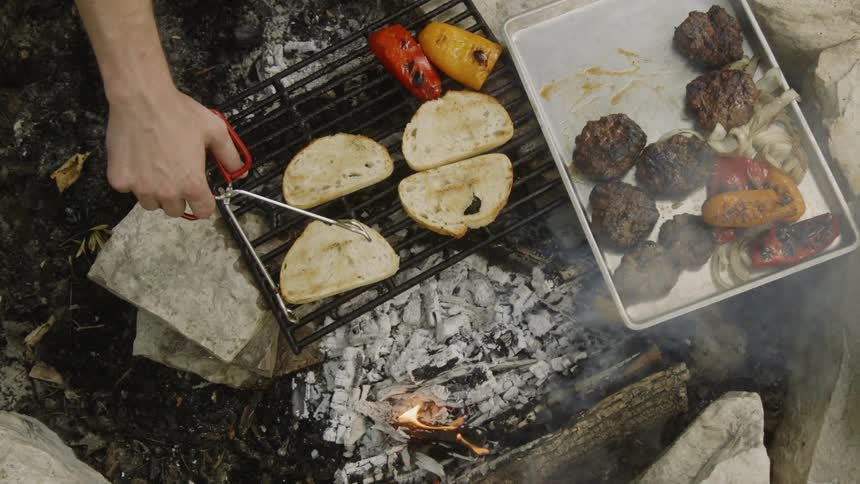 A man uses tongs to move bread around on a grill outdoors