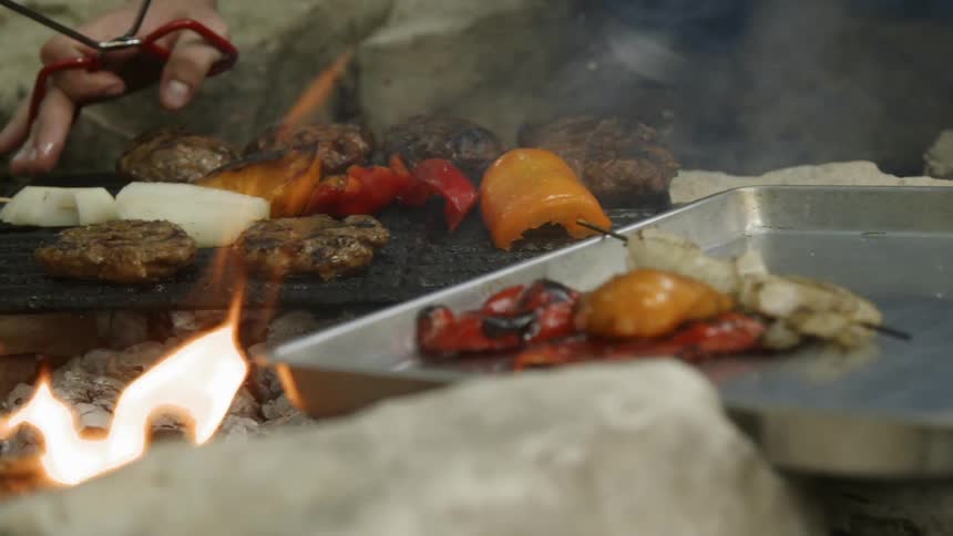 A person places more food on a flaming grill