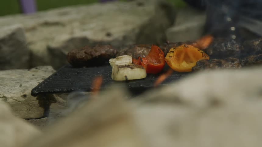 A person uses tongs to move food on a flaming grill
