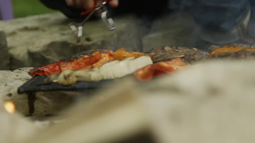 A man turns meat and veggies on a grill with tongs
