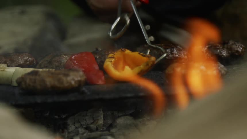 A man uses tongs to flip a pepper on a flaming grill