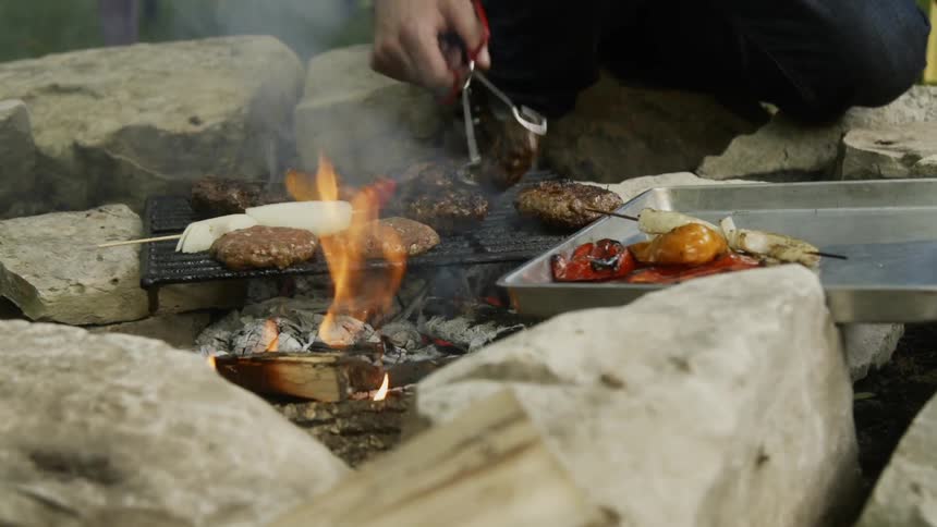 Man flips the grilling burgers with tongs