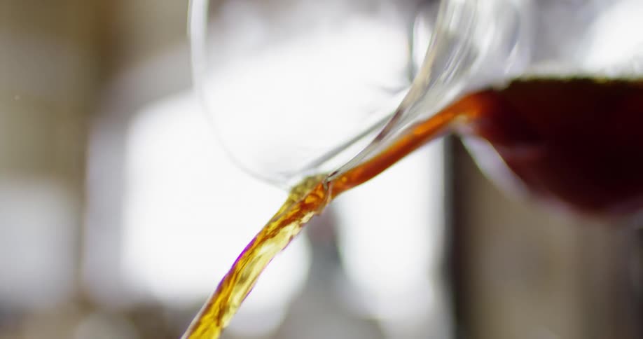 A brown liquid is being poured out of a glass container