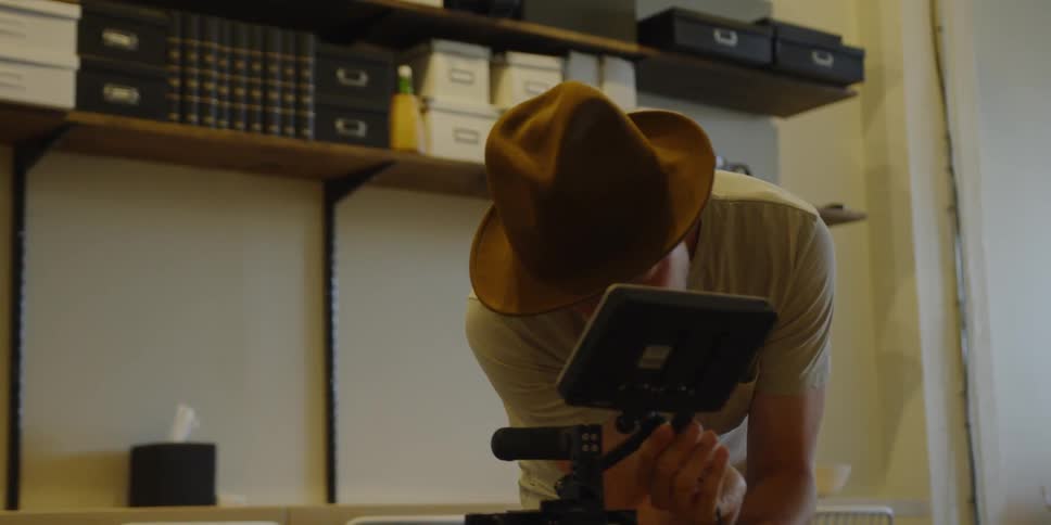 Man wearing a brown hat attaches a cord to a small screen