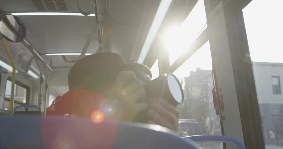A man uses his camera while traveling through a city on a bus
