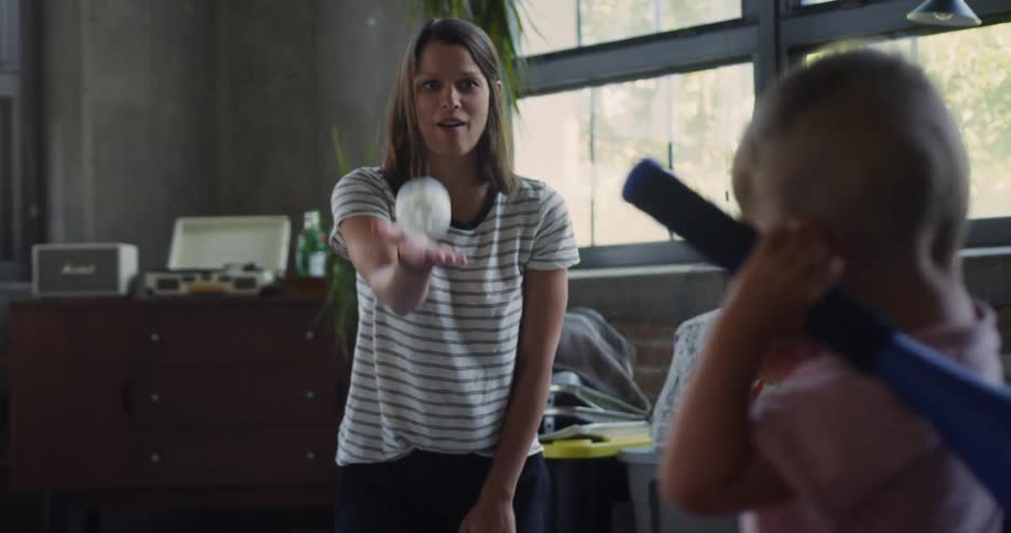 Woman tosses a ball to a little boy holding a bat