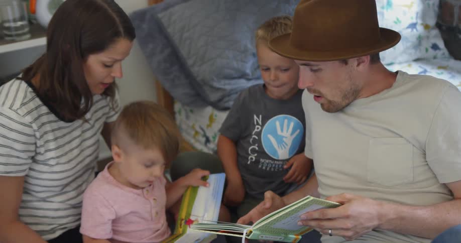Man and woman read a book to two boys